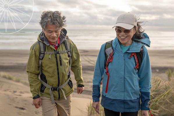 middle-aged couple in rain jackets walking on the beach